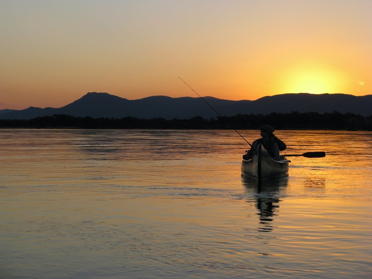 A canoeist paddling on calm water as the African sun sets